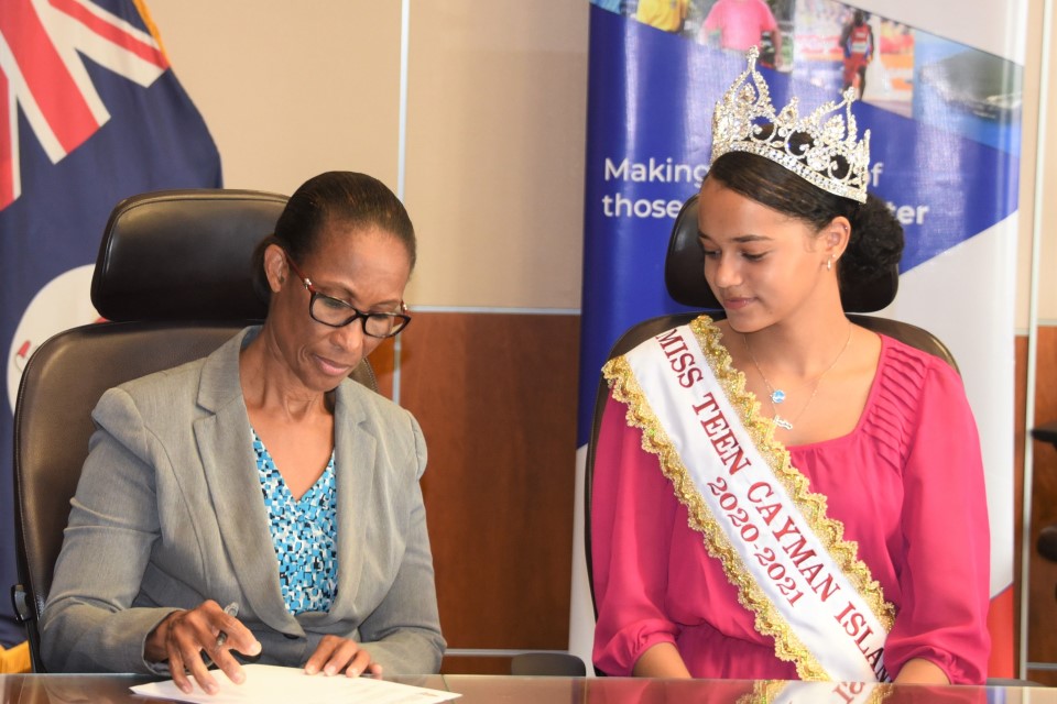 Miss Teen Cayman Jada Bodden watches as MEYSAL Acting Chief Officer Lyneth Monteith signs the scholarship contract.